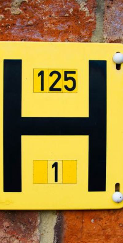 Black H on a yellow square plaque, placed on a brick wall and a metal cover in the ground with an embossed H. 