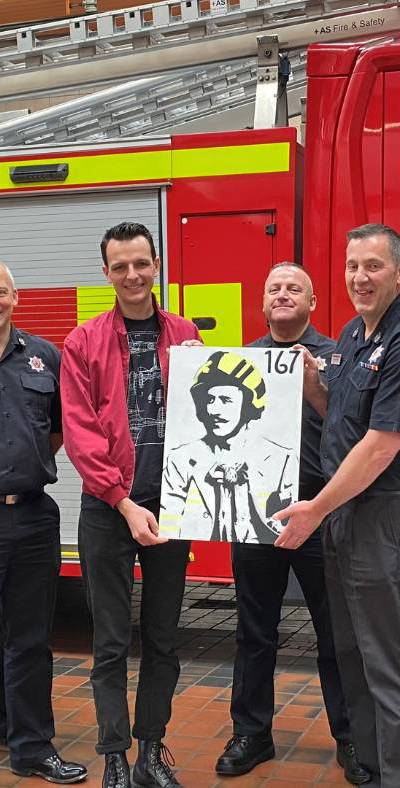 A group of firefighters and an artist standing in front of a fire truck holding a painting