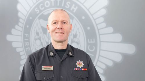 David Farries in uniform in front of a grey SFRS crest