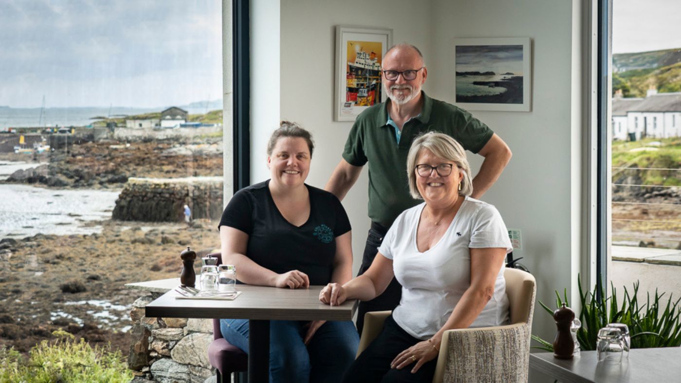 Laura, Kevin, and Julie Oliphant around a table with views of the coast