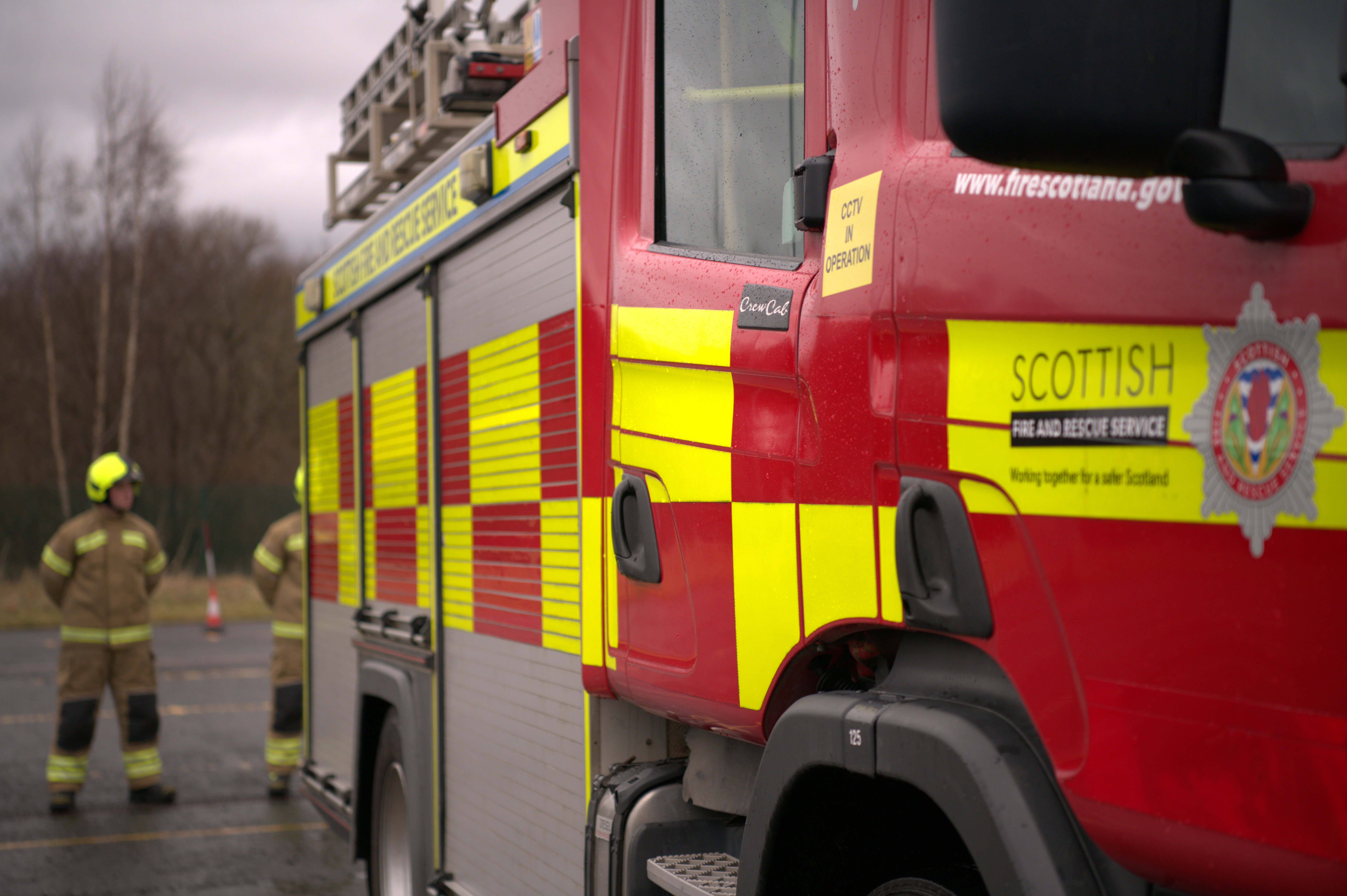 Picture of a fire engine with a firefighter in the background with their hands behind their back.