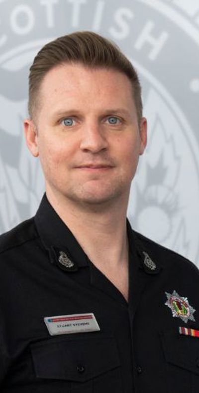 Stuart Stevens in uniform in front of a grey SFRS crest