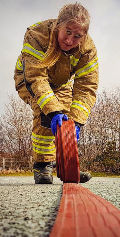 Female firefighter rolling a red hose