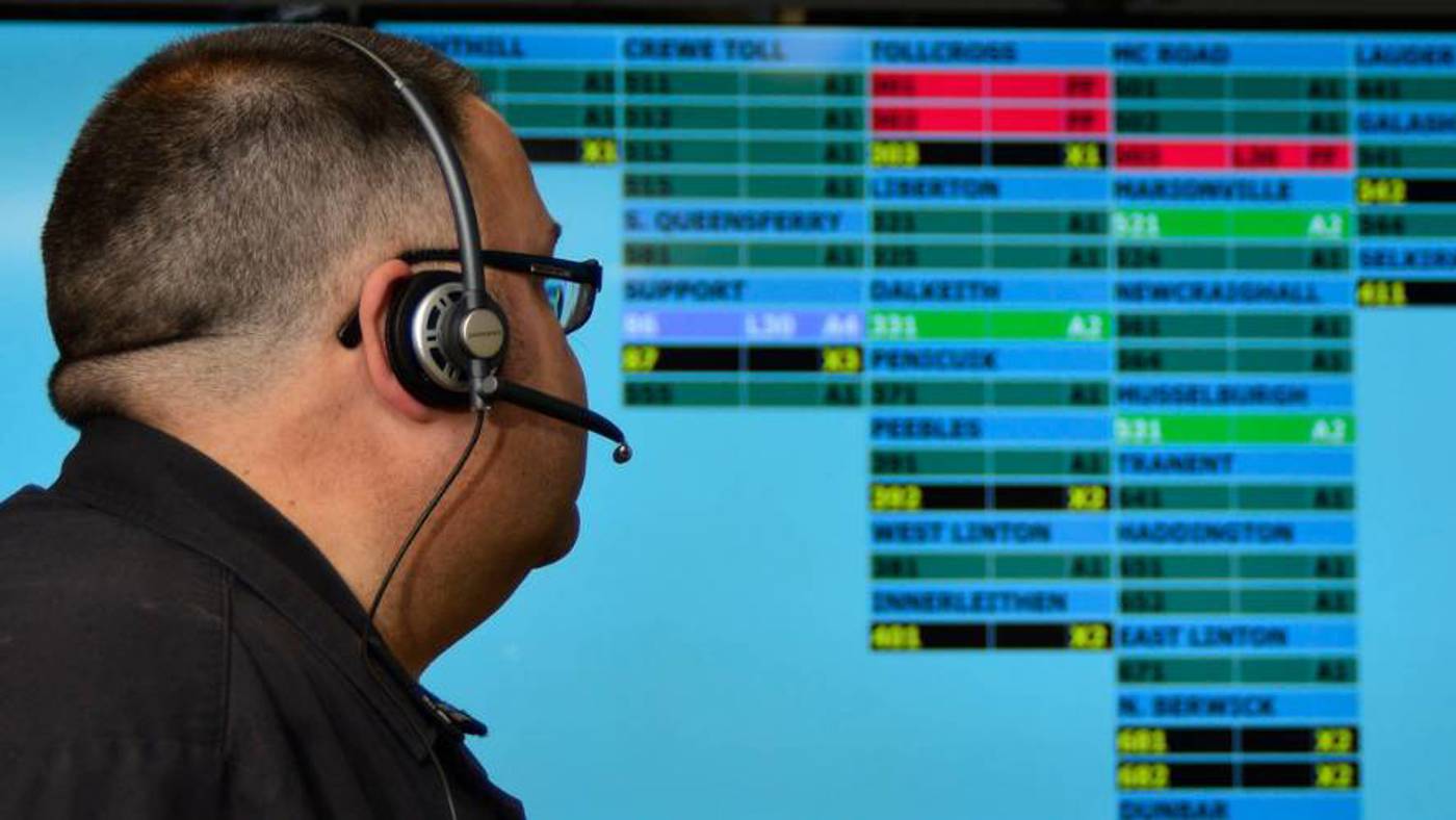 Control firefighter with a headset on sitting in front of a screen with lots of boxes of place names