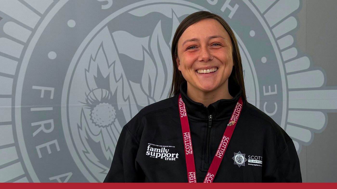 A smiling woman dressed in a fire and rescue jacket embodies commitment to her role in public safety.