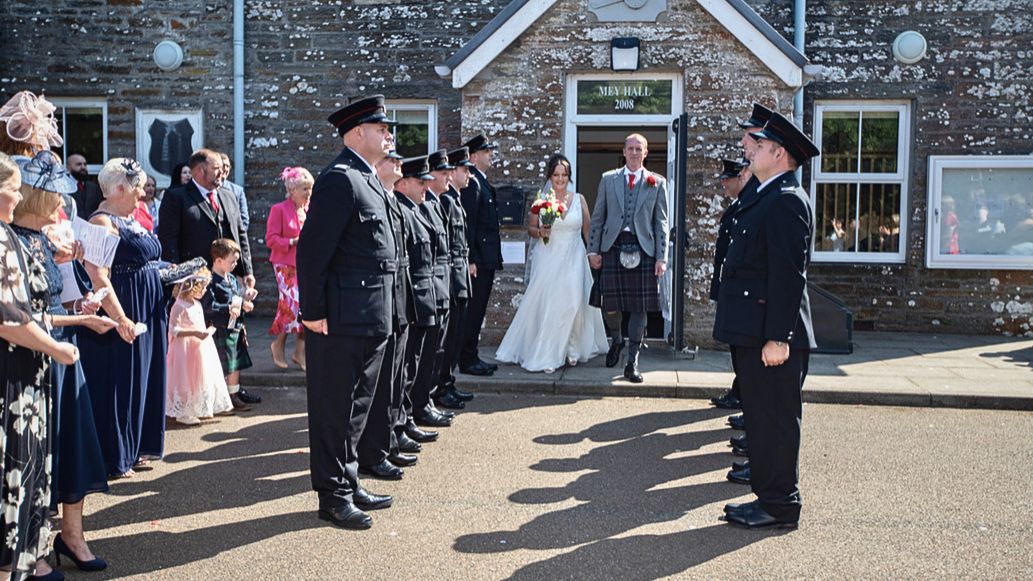 a bride and groom walking out of an old building through a line of firefighteres dressed in black uniforms