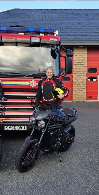 Two firefighters standing next to motorbikes and a fire appliance