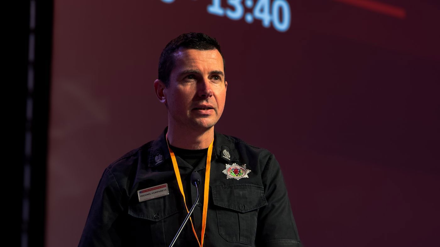 A uniformed man stands at a podium, speaking to an audience at a conference.