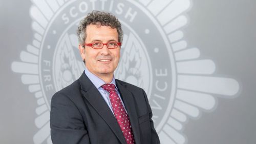 Head and shoulders image of Board member Tim Wright smiling in front of a grey SFRS crest