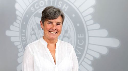 Head and shoulders image of Board member Fiona Thorburn smiling in front of a grey SFRS crest